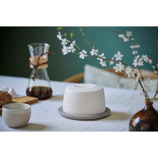 Beurrier en céramique sur une table avec des fleurs et une cafetière.