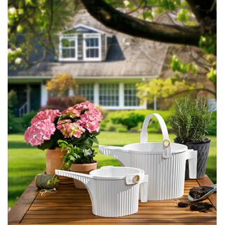 Deux arrosoirs en blanc et des fleurs sur une table au jardin
