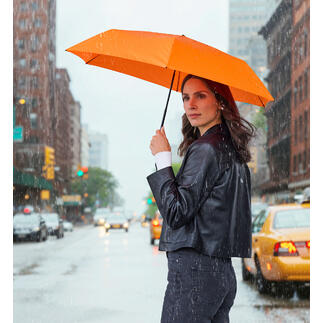 Femme tenant un parapluie orange en pluie, debout dans la rue.