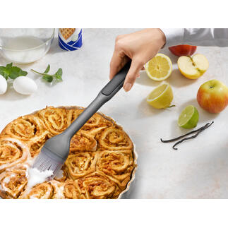 Main avec un pinceau à pâtisserie qui badigeonne un gâteau à la cannelle chaud.