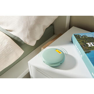 Réveil vibrant en vert doux, sur une table de nuit à côté d'un livre et d'une couette.
