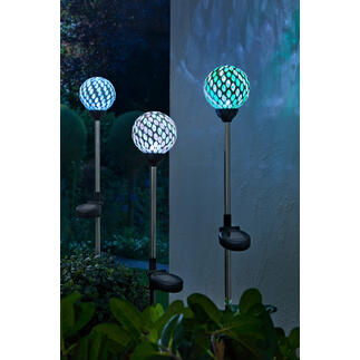 Trois piquets solaires avec des lampes en mosaïque colorées dans le jardin.