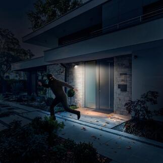 Homme tentant de cambrioler une maison dans l'obscurité alors qu'une imitation de caméra solaire éclaire.