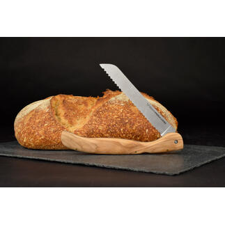 Couteau à pain pliable avec manche en bois d'olivier à côté d'un pain sur un fond noir.