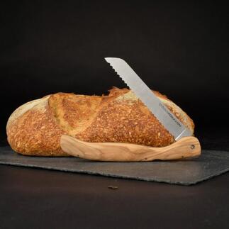 Couteau à pain pliable avec manche en bois d'olivier à côté d'un pain sur un fond noir.