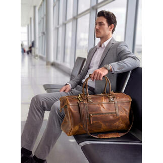 Homme assis à l'aéroport avec un weekender en cuir de buffle à côté.