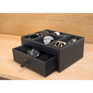Boîte de rangement noire en cuir contenant divers accessoires comme des montres et des lunettes.