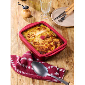 Plat à four rouge avec couvercle, rempli d'un plat de haricots, sur une table en bois.
