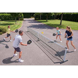 Une famille joue au pickleball en plein air, avec un filet et des balles.