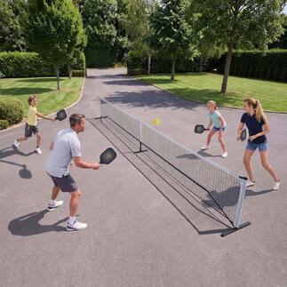 Une famille joue au pickleball en plein air, avec un filet et des balles.