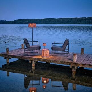 Table de jardin avec éclairage LED au bord de l'eau, entourée de chaises.
