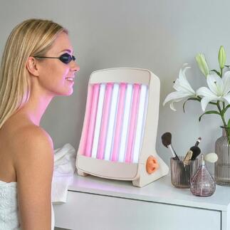 Bronzer facial avec des lampes roses et bleues, placé sur une table à côté de produits cosmétiques.