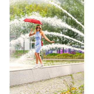 Femme avec un parapluie rouge se tient devant une fontaine.