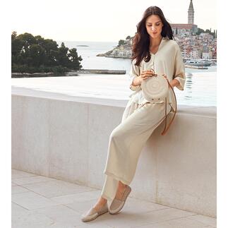 Femme assise sur un mur, portant des vêtements clairs et des espadrilles.