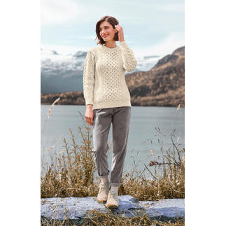 Femme en pull Merino-Aran blanc en laine au bord de l'eau avec vue sur les montagnes