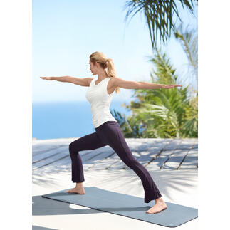 Femme en pose de yoga portant un haut en cascade blanc et un pantalon de yoga sur une terrasse en bois à l'extérieur.