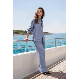 Femme en chemise bleue et pantalon se tient sur un bateau au bord de la mer.