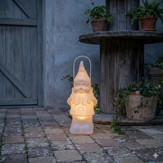 Gnome de jardin LED avec lumière douce, placé sur un sol en briques près de pots de fleurs.