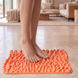 Mat de réflexologie plantaire goFit en orange vif, sur un sol clair avec des pieds dessus.