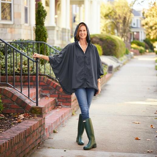 Femme portant un poncho de pluie noir de style sportif avec capuche, debout à l'extérieur.