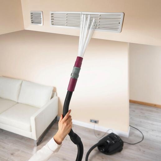Main avec accessoire d'aspirateur nettoyant une grille de ventilation.