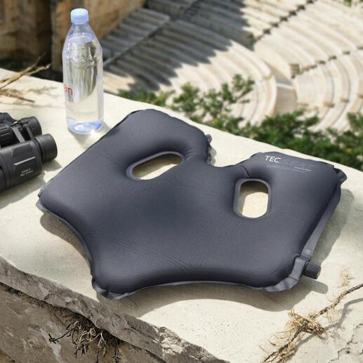 Fauteuil SoftAirSeat confortable sur une pierre avec une bouteille d'eau et des jumelles.
