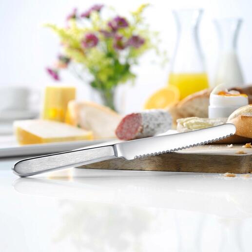 Couteau à pain en acier inoxydable sur une table avec du pain et des fleurs.