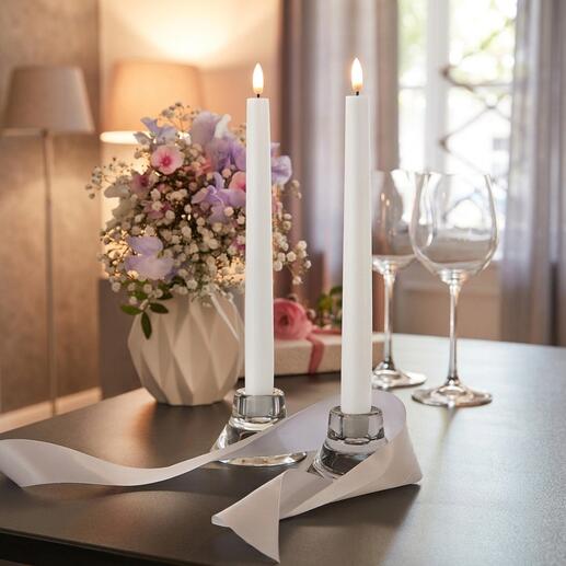 Deux bougies LED en forme de bâton dans un environnement décoratif près de fleurs.