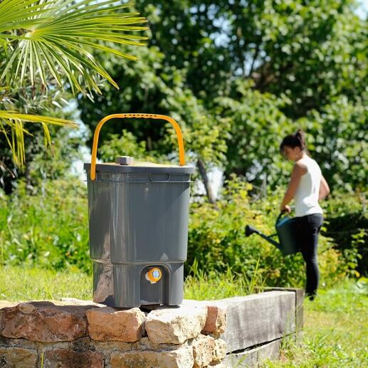 Préparateur de fertilisant liquide BioMix dans un jardin, femme travaillant en arrière-plan.