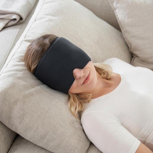Femme avec une compresse noire sur les yeux se détend sur un canapé.