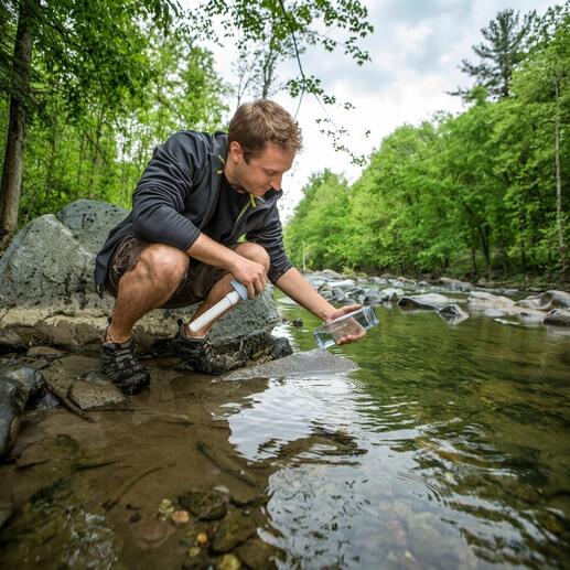 Homme remplissant de l'eau d'un ruisseau avec une bouteille filtrante
