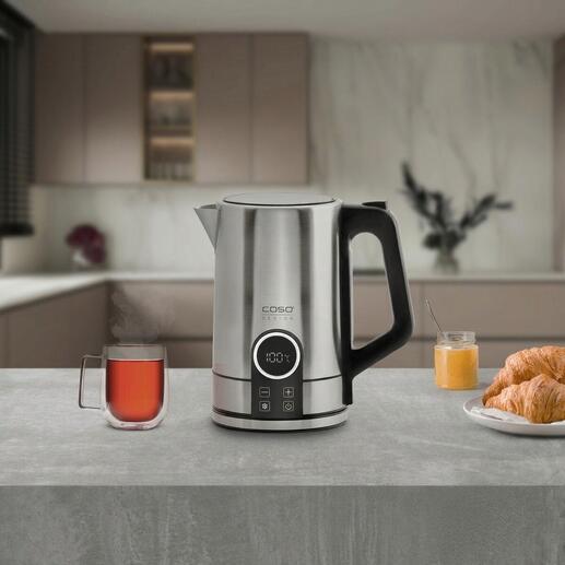 Bouilloire en acier inoxydable moderne sur un plan de travail avec une tasse de thé et un croissant.