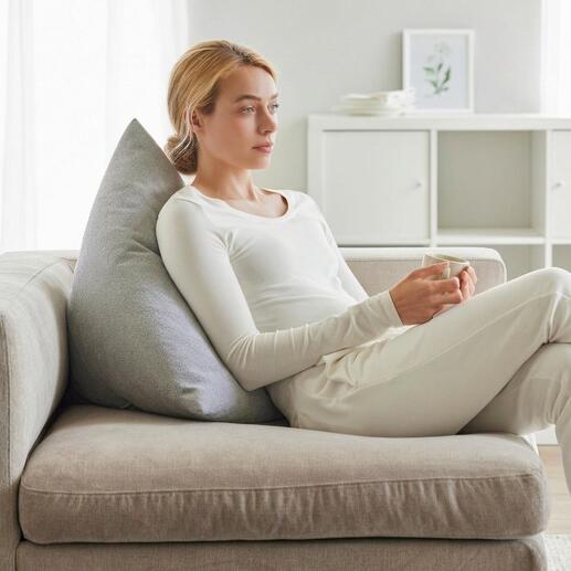 Femme avec un coussin de dos gris assise détendue sur un canapé.