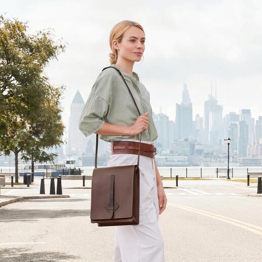 Femme portant un sac à carte Chiarugi marron sur l'épaule devant une vue de la ville.