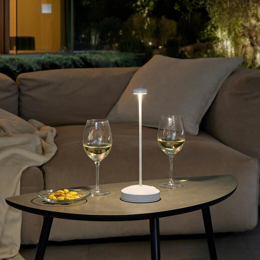 Lampe de table design avec batterie sur une table, entourée de verres à vin et de collations.