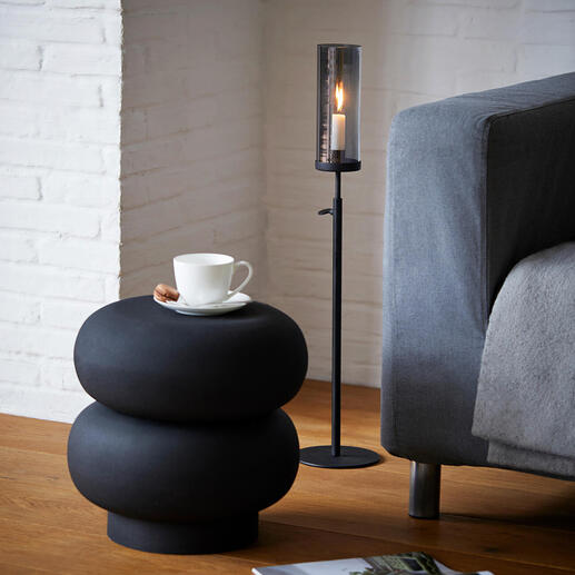 Lanterne réglable à hauteur à côté du canapé, sur une table basse noire avec une tasse et un magazine.