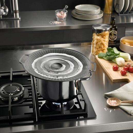 Casserole avec couvercle anti-éclaboussures sur la cuisinière, pâtes et légumes à côté.