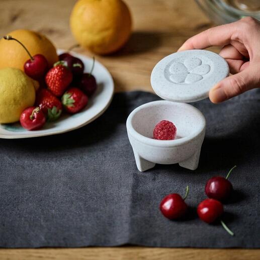 Piège à mouches en porcelaine avec une main ouvrant le couvercle et des fruits sur la table.