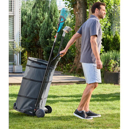 Homme tirant un chariot de jardin pliable avec des feuilles dans le jardin.