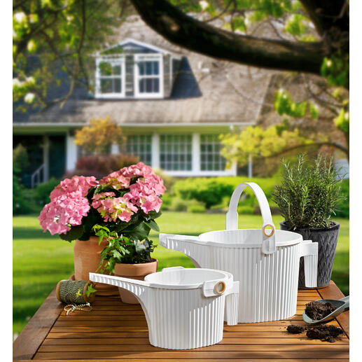 Deux arrosoirs en blanc et des fleurs sur une table au jardin
