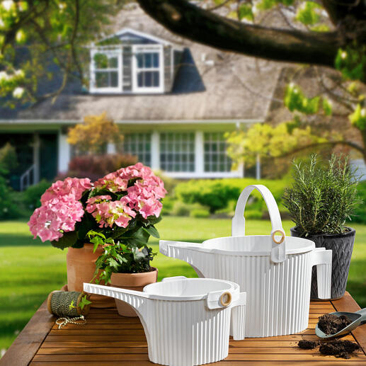 Deux arrosoirs en blanc et des fleurs sur une table au jardin