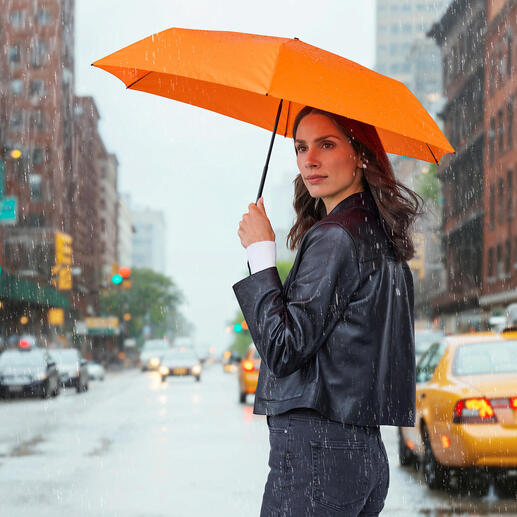 Femme tenant un parapluie orange en pluie, debout dans la rue.