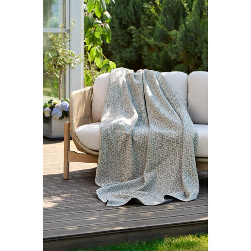 Couverture réversible en jacquard posée sur un banc de jardin.