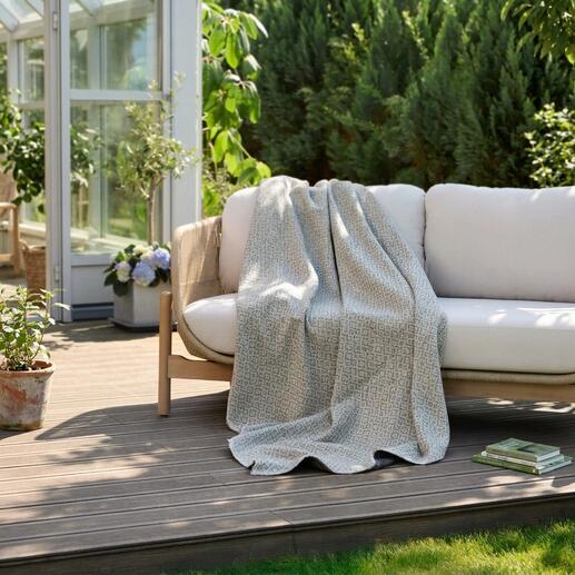 Couverture réversible en jacquard posée sur un banc de jardin.