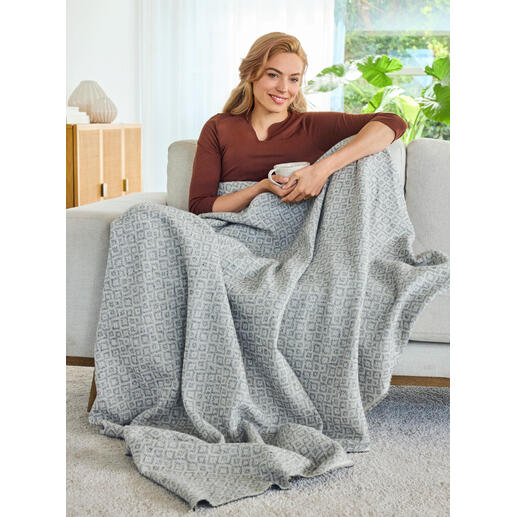 Idéale également comme couverture légère pour des heures douillettes sur le canapé. Femme assise sur un canapé enveloppée dans une couverture en jacquard.