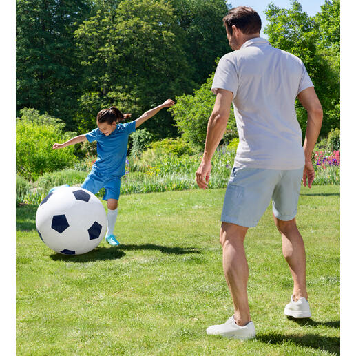Un garçon joue avec un grand ballon de football dans le jardin.