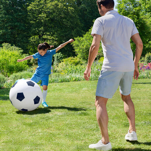 Un garçon joue avec un grand ballon de football dans le jardin.