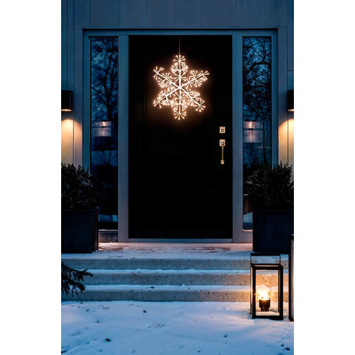 Flocon de neige LED éclairé à l'extérieur, suspendu devant une porte d'entrée.