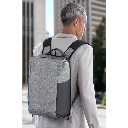 Sac à dos anti-vol La combinaison parfaite de sécurité et de style : le sac à dos anti-vol moderne. Homme avec un sac à dos antivol gris sur le dos devant un paysage urbain.