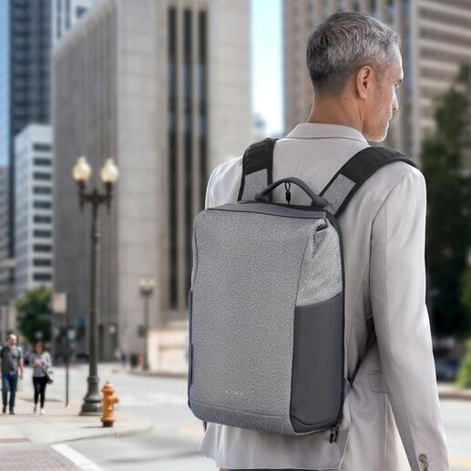 Homme avec un sac à dos antivol gris sur le dos devant un paysage urbain.
